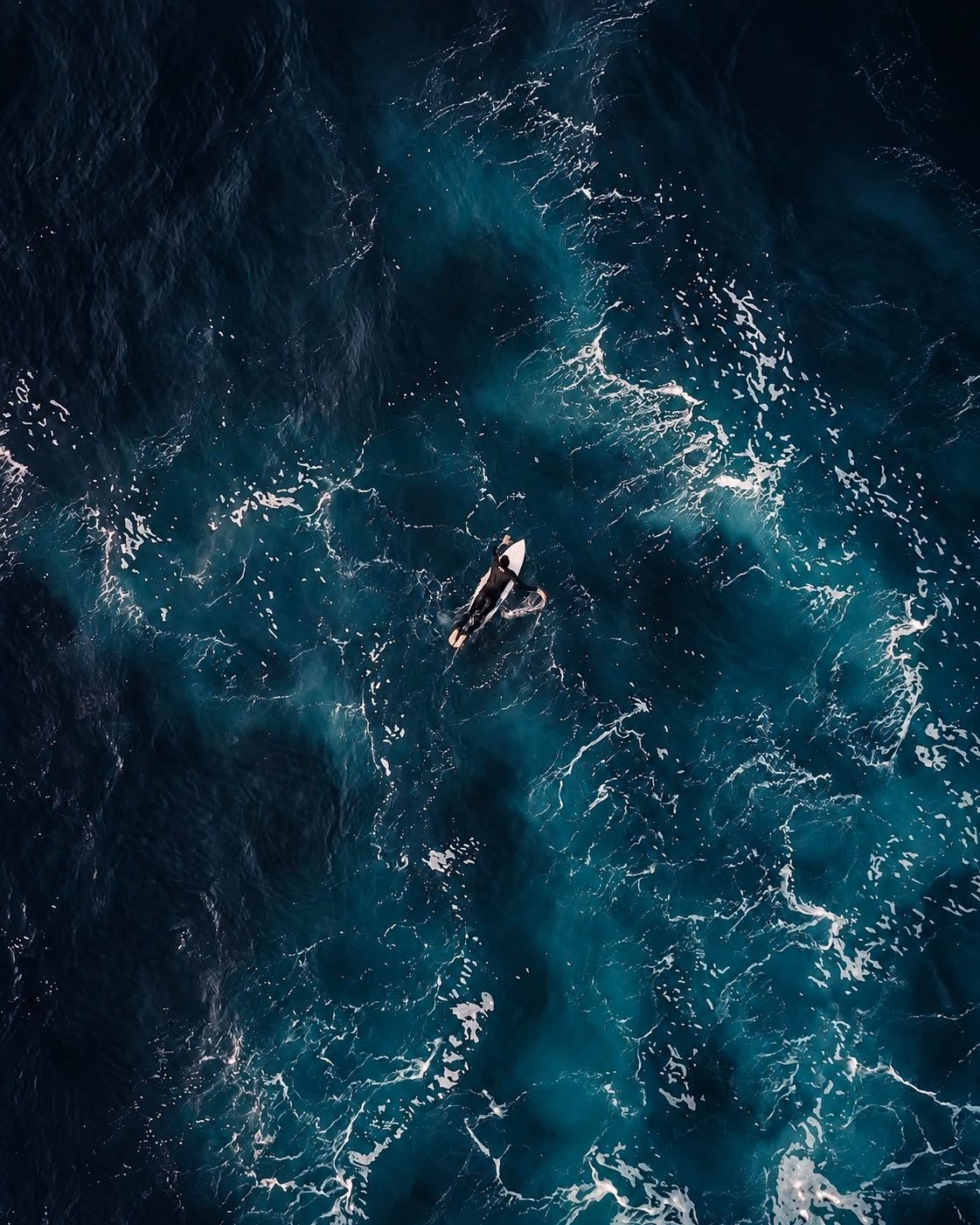 Lone surfer paddling in deep blue water